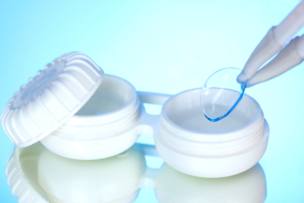 contact lenses in containers and tweezers on blue background